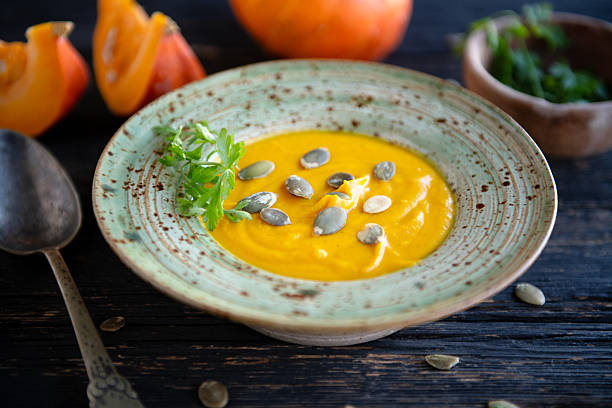 A shallow ceramic bowl filled with creamy pumpkin soup, garnished with fresh herbs and pumpkin seeds, photographed in a warm rustic kitchen setting.