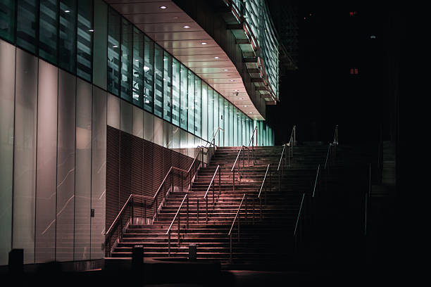 An illuminated staircase leads up to a modern building at night, with reflections on the glass exterior and a dark sky.
