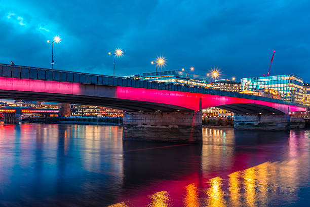 London bridge illuminated with pink light reflecting on the calm river thames at twilight