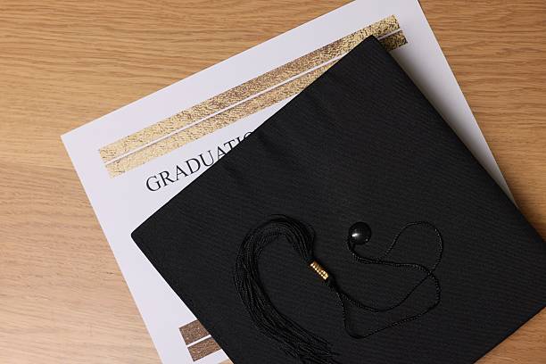Graduation cap and diploma on wooden table, top view