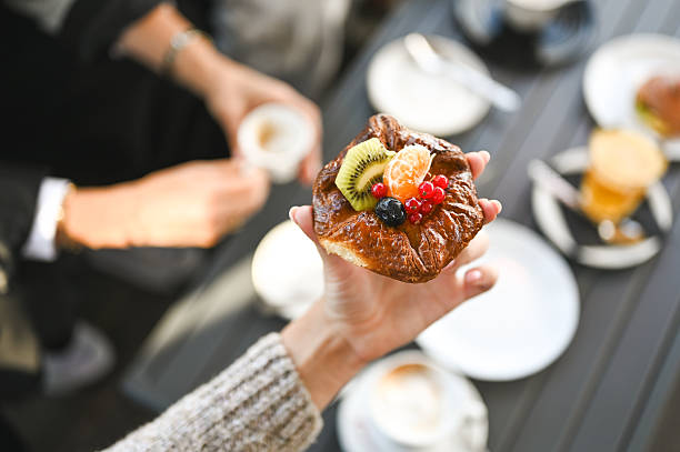 Hand holding a fresh fruit danish while enjoying coffee and breakfast with friends