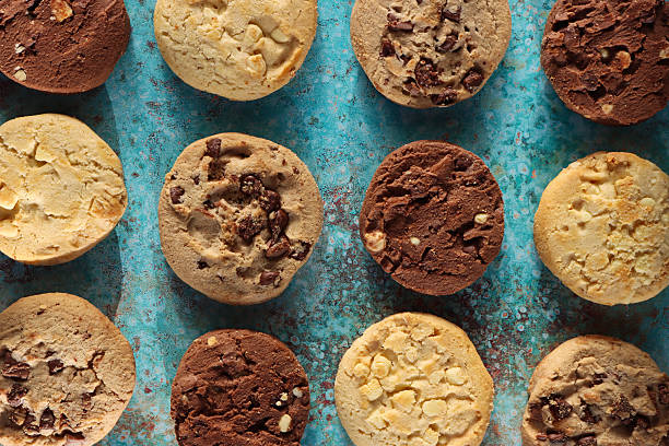 istock Full frame image of rounds of chocolate chip shortbread biscuits flat lay, rows of alternating triple chocolate chip, milk chocolate chip and white chocolate chip cookies, mottled blue-green background, elevated view 2246585905