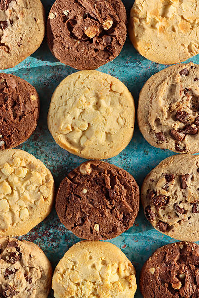 istock Full frame image of rounds of chocolate chip shortbread biscuits flat lay, rows of alternating triple chocolate chip, milk chocolate chip and white chocolate chip cookies, mottled blue-green background, elevated view 2246586009