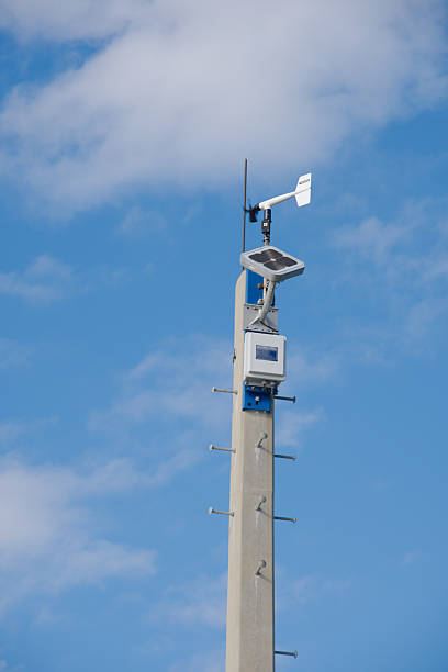 A modern weather station on a tall pole featuring a solar panel and anemometer against a clear blue sky, emphasizing outdoor technology and meteorological data collection.