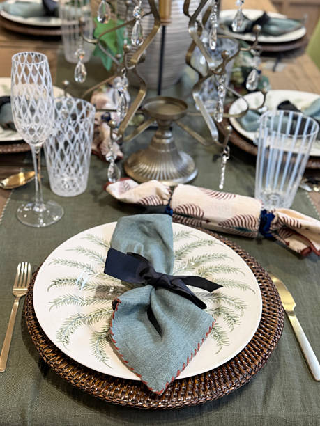 istock Image of dining table place setting, fern patterned dinner plates, forks and knives, cloth Christmas crackers, etched drinking tumblers and wine glasses, brass candle holder with hanging crystals, place mats, tablecloth, elevated view, focus on foreground 2246600315