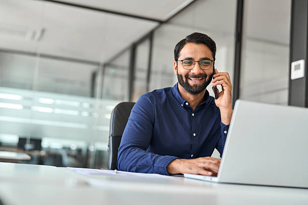 istock Happy Indian businessman merchant calling on cell phone using laptop in office. 2246601176