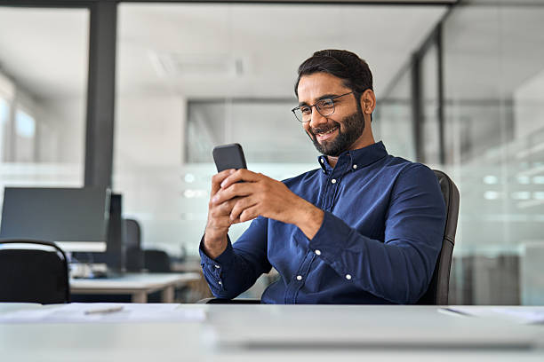 istock Happy busy Indian businessman employee using cell phone working in office. 2246601189