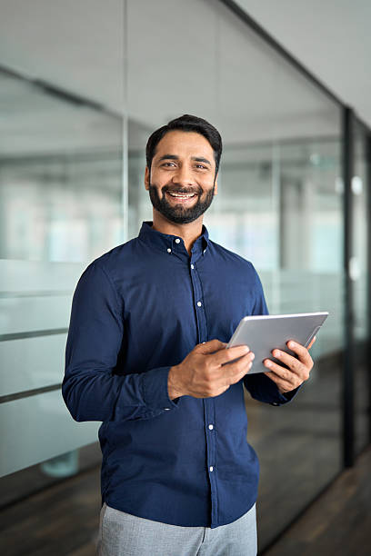 istock Happy Indian businessman using tab working standing in office. Vertical 2246601248