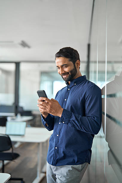 istock Busy Indian businessman using mobile phone working standing in office. Vertical 2246601262