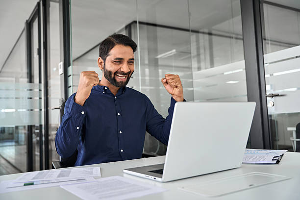 istock Happy Indian business man winning prize online working using laptop in office. 2246601321
