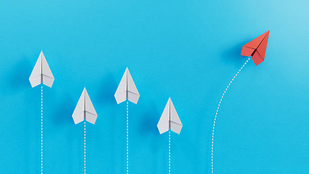 istock Red Paper Airplane Taking a Distinct Path Away from White Counterparts on Blue Background 2246609976