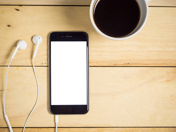istock Blank screen smartphone with coffee and earphone on wooden table. 2246612967