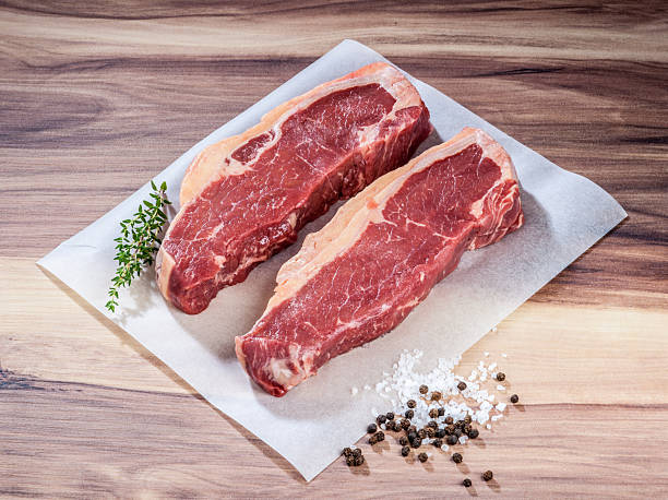 Raw Sirloin Steaks with Thyme, Sea Salt, and Peppercorns on Wooden Surface