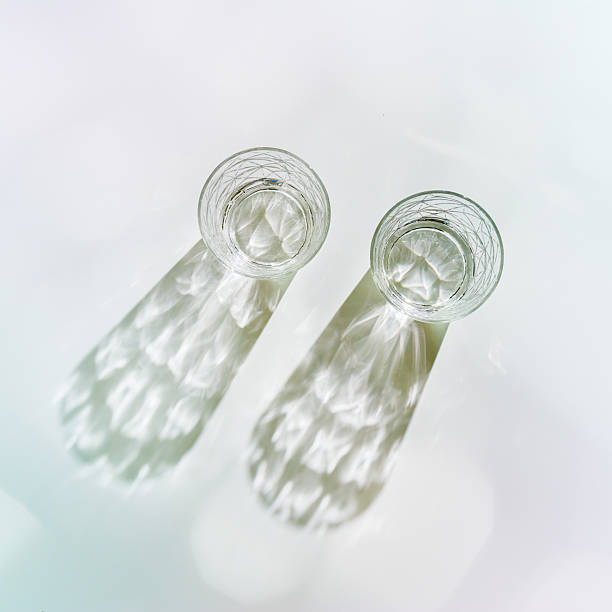 istock Water Glasses with Shadows and sunlight Reflection on white background, colored toned photo minimal style, aesthetic top view summer still life, refraction throug crystal shine cups, caustics 2246616597