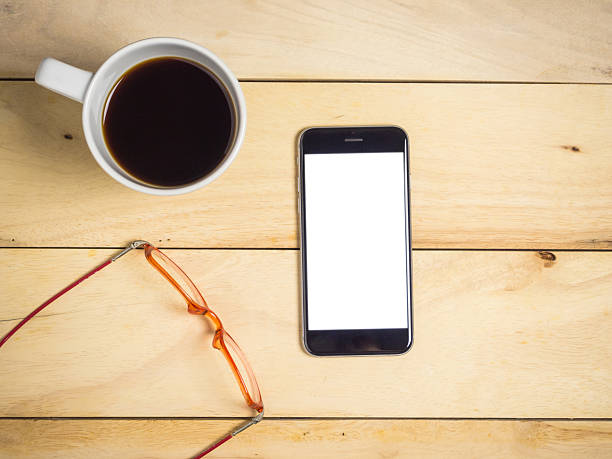 istock Blank screen smartphone with coffee and glasses on wooden table. 2246632449