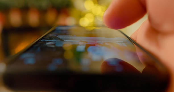Finger tapping smartphone screen, navigating social media timeline with festive blurred lights, revealing digital connectivity and lifestyle interaction