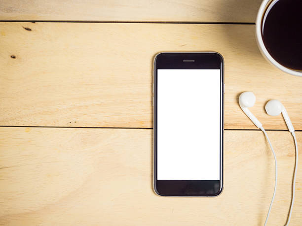 istock Blank screen smartphone with coffee and earphone on wooden table. 2246634565