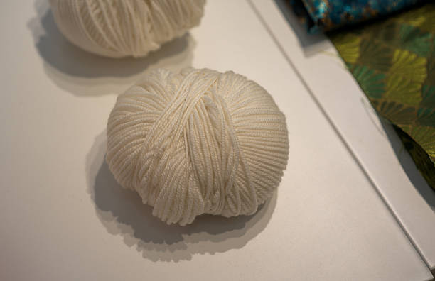 White yarn balls placed on a white tabletop with soft shadows and a colorful background partially visible