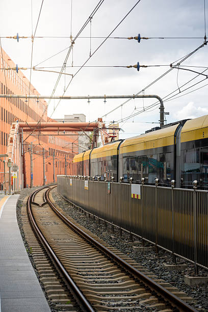 istock A Yellow Train Approaching the Platform at a Modern Urban Railway Station with Overhead Electric Lines and Industrial Architecture in the Background 2246649472