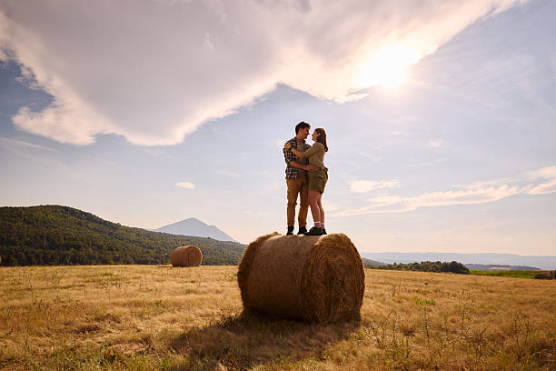 Happy couple in love talking while standing embraced on a hay bale during spring day at the countryside.