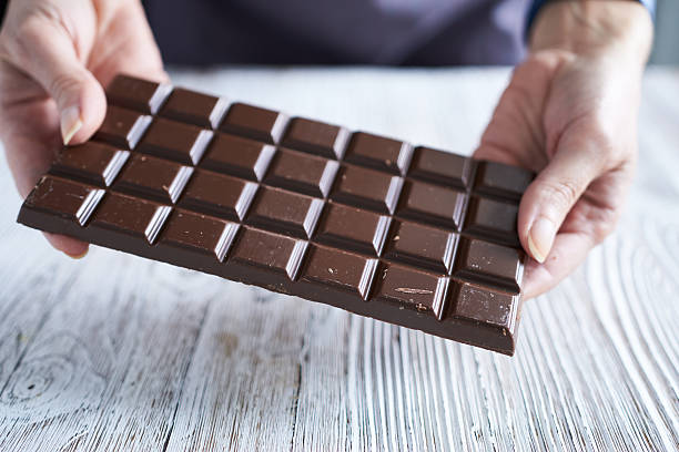 istock Woman's hands holding a chocolate bar on a white wooden background. 2246655679