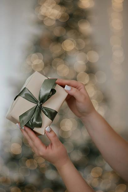 istock Hands Holding Gift Box with Satin Bow by Christmas Tree 2246656455