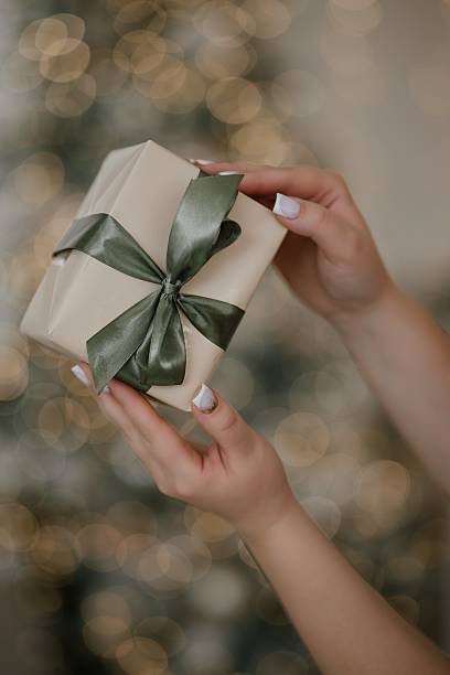 istock Hands Holding Gift Box with Satin Bow by Christmas Tree 2246656544