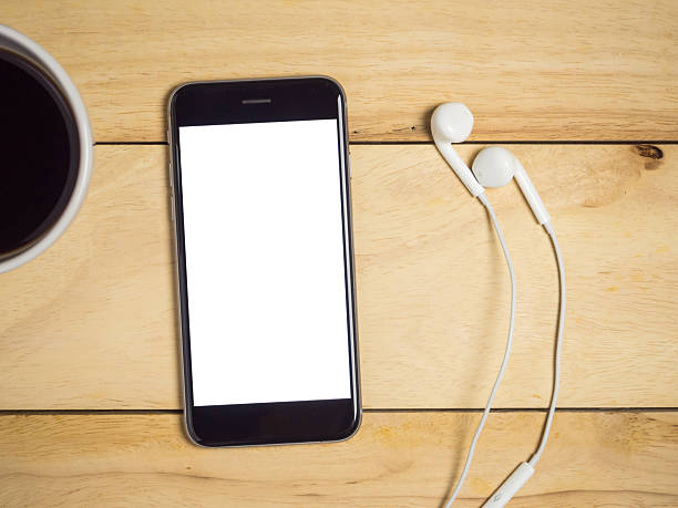 Blank screen smartphone with coffee and earphone on wooden table.