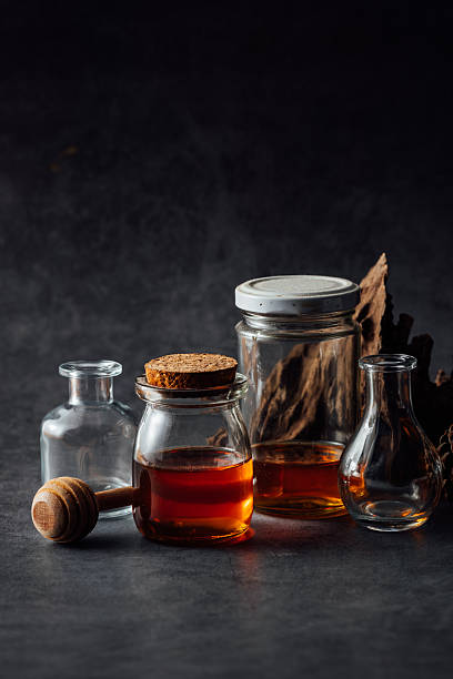 Glass jars with honey and syrup on dark textured background