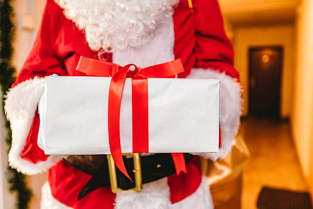 Close-up of a Santa Claus holding a gift while standing in a building hallway.