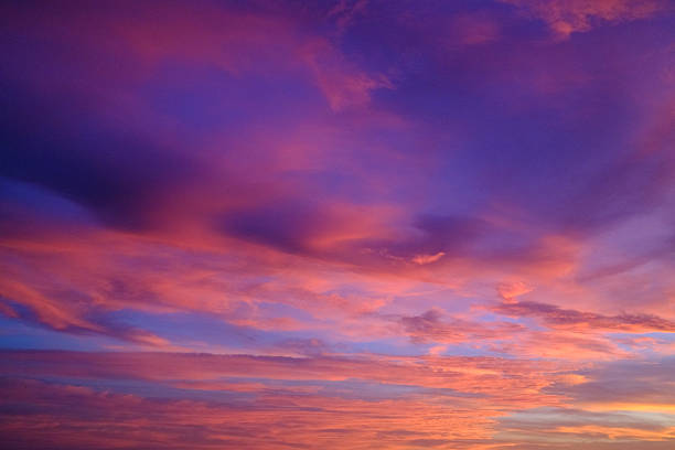 Sunset sky streaked with dramatic purple, pink and orange clouds, a vibrant twilight cloudscape casting warm light across a peaceful, serene horizon