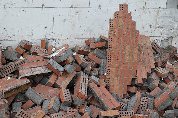A close-up view of a large pile of red bricks and debris, some with mortar attached, stacked against a weathered white wall. Symbolizes construction, demolition, or aftermath of destruction.