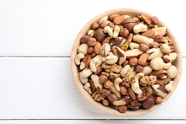 istock Mix of different nuts in bowl on white wooden table, top view. Space for text 2246659354