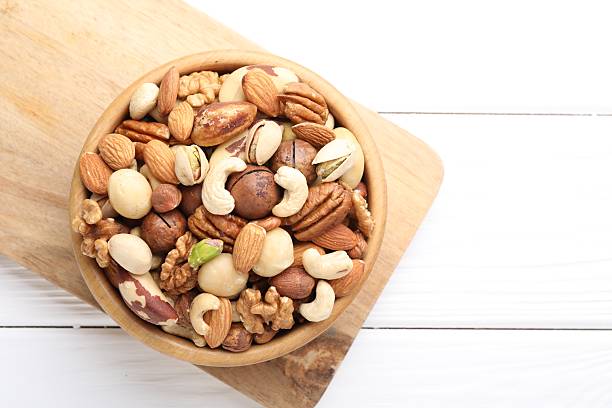 istock Mix of different nuts in bowl on white wooden table, top view. Space for text 2246659367