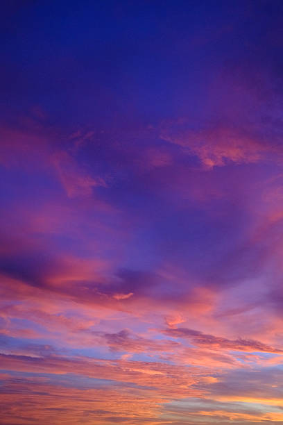 Evening sky painted with vibrant purple, pink and orange cumulus clouds, a serene twilight gradient casting warm, dramatic light over a peaceful, non-urban horizon