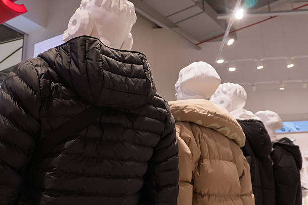 A group of mannequins dressed in puffer jackets is displayed indoors under bright lighting. The mannequins are arranged in a line, showcasing different colored winter outerwear.