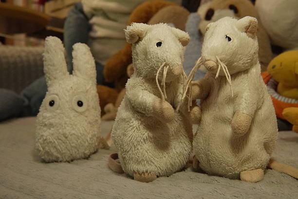 Two small gray plush mice (or hamsters) standing next to a plush rabbit against a blurred background of toys. High quality photo