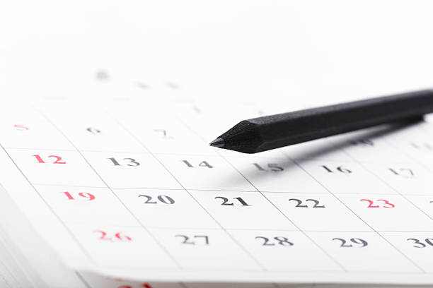 A black pencil rests on a calendar as specific dates are highlighted in a clean space.
