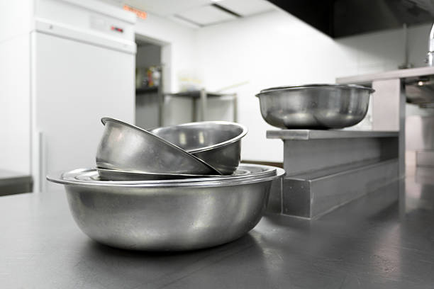 Stacked metal mixing bowls sit on a stainless steel counter in a well-lit kitchen.