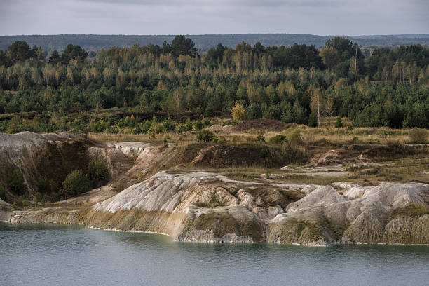 Turquoise water bordered by eroded chalk terrain and mixed forest, under a cloudy autumn sky.