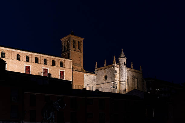 Tordesillas town showing historic buildings, including a prominent bell tower and church facade, subtly illuminated against the deep blue night creating a serene and timeless atmosphere