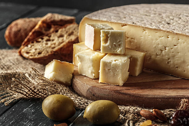 Cheese displayed on a wooden board with bread and olives in a rustic setting