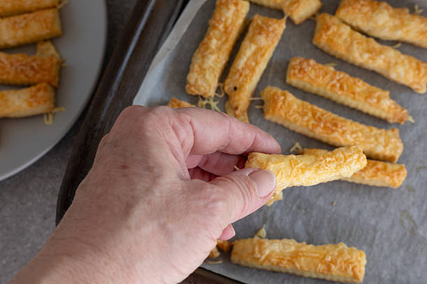 istock hand holding a cheese stick above a baking sheet 2246670416