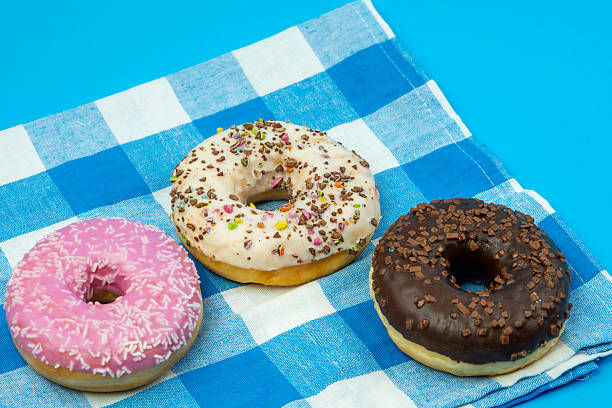 Colorful donuts with pink, white and chocolate icing rest on a checkered napkin positioned against a blue background