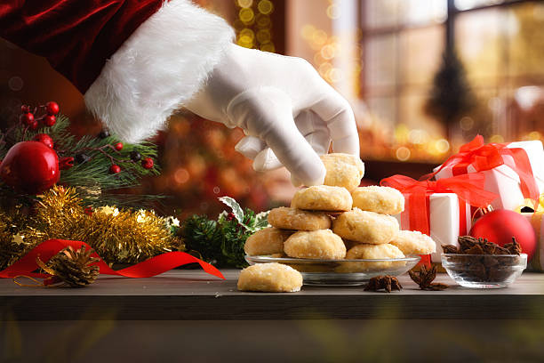 Santa's hand taking cookie on Christmas table with Christmas decorations in a warm room with a window decorated with Christmas decorations. Front view.