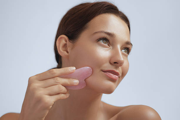 istock Young Woman Using Pink Gua Sha Stone On Face For Skincare And Lymphatic Drainage 2246678049
