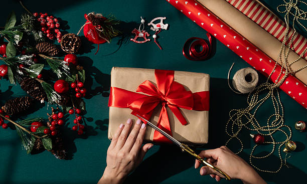 istock Hands trimming red ribbon bow on wrapped Christmas gift 2246678068