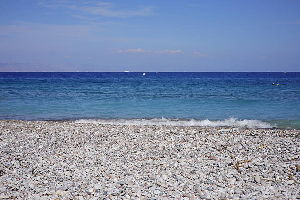 Scenic view of a tranquil bay in the coastal village of Sissi near Malia, Crete, Greece. The image captures the crystal-clear turquoise waters of the Mediterranean Sea, framed by rocky shores and a breakwater extending into the sea with a small beacon.