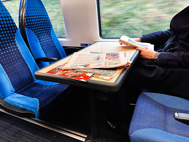 Manchester, UK - October 04, 2025: A passenger sits at a table on a moving train with newspapers spread out in a blue seating carriage.