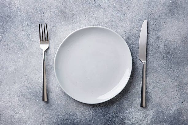 istock Empty white plate with a fork and knife on a grey stone background. Flat lay. Copy space. Top view. 2246700401